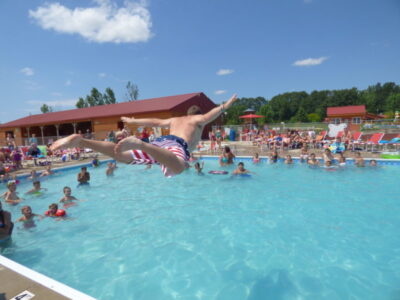 Family enjoying the swimming pool at Jellystone Park™ with guests jumping and playing in the water