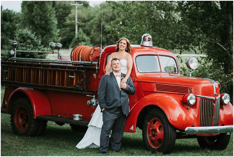 Bride and groom posing by a vintage red fire truck at a wedding at The Barn at the Resort at Jellystone Park South Haven
